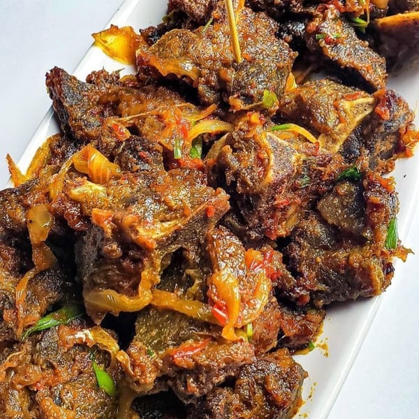 Close-up of Afra Grill's African grilled meat, glistening with sauce, onions, and green herbs.