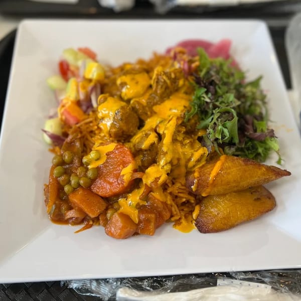 Afra Grill's African dish with meat, rice, vegetables, plantains, and salad on a white plate.