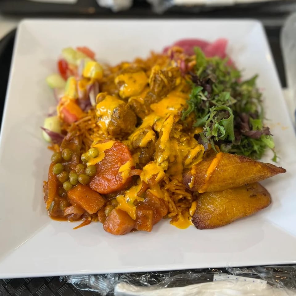 Afra Grill's African dish with meat, rice, vegetables, plantains, and salad on a white plate.