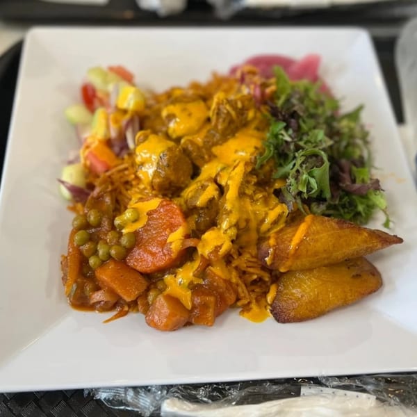 Afra Grill's African dish with meat, vegetables, plantains, and a side salad on a white plate.
