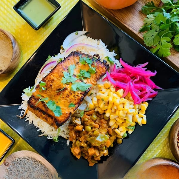 Afra Grill's grilled salmon with rice, corn, vegetable stew, and pickled onions on a black plate.